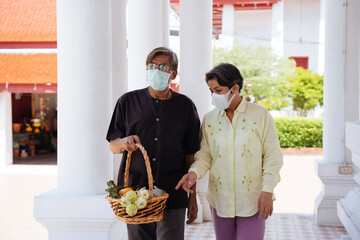 Asian senior elderly couple wear mask in a temple to make a merit.