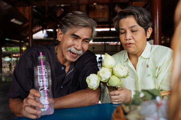 Grandparents make a merit woth lotus flower in temple.