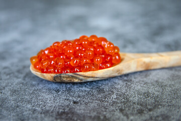 Red caviar in a wooden spoon on a blue background. Close-up.