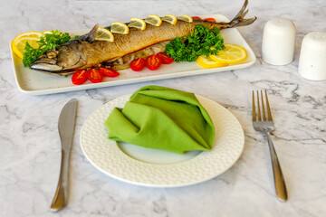 Oven baked mackerel on a white plate with lemon and cherry tomatoes.