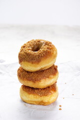 Donat or Donut or Doughnut as circle with hole sweet bread topped with caramel and biscuit crumbs. Pile of doughnut in white shiny background