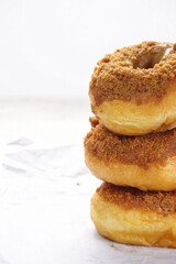 Donat or Donut or Doughnut as circle with hole sweet bread topped with caramel and biscuit crumbs. Pile of doughnut in white shiny background
