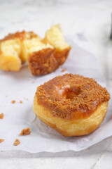 Donat or Donut or Doughnut as circle with hole sweet bread topped with caramel and biscuit crumbs. Selective focus, white shiny background