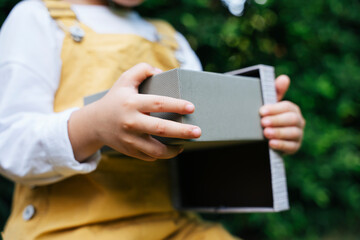 Kid opening grey birthday gift in a party outdoors at yard