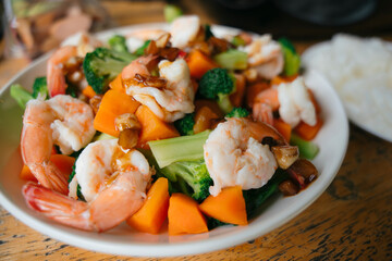 Stir fry seafood with shrimp and vegetables on wooden plate.