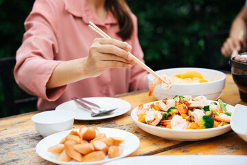 Woman using chopstick eating stir fry and sausage.