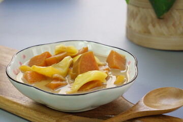 A plate of Kolak Ubi Nangka or Indonesian dessert made from Sweet Potato and Jack fruit as a compote. Based on coconut milk, palm sugar and Pandanus leaves in isolated gray background