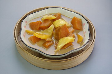 Top view of Kolak Ubi Nangka or Indonesian dessert made from Sweet Potato and Jack fruit as a compote. Based on coconut milk, palm sugar and Pandanus leaves in isolated gray background