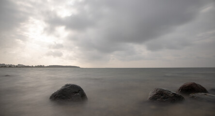 Fototapeta na wymiar Es ist ein trüber, ungemütlicher Tag an der Küste eines Meeres. Große Steine liegen am Ufer. Dichte Wolken sind am Himmel