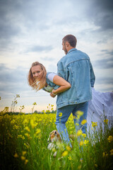 Young beautiful couple having fun on natural background. Date of guy and girl on a green field with glass and flowers in cloudy summer day. Yound family having rest together