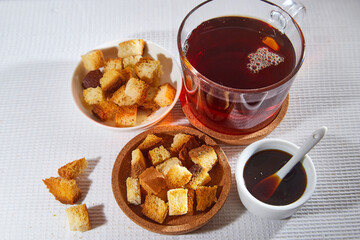 Square toasted pieces of homemade delicious rusk, hardtack, Dryasdust, zwieback, Liquid honey in a saucer and black tee in a cap on a white tablecloth.