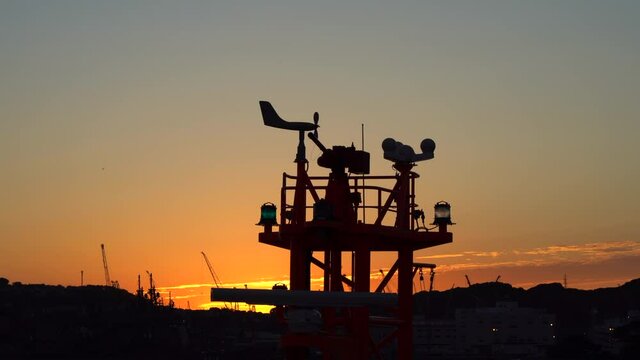 weather station on top of the port ship. the blades of the anemometer rotate against the backdrop of sunset and port cargo cranes