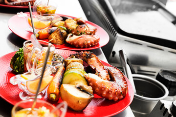Red plate with grilled octopus tentacles served with lemon and vegetables