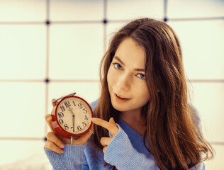 Beautiful young woman showing time on alarm clock