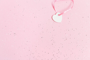 White small heart on pink paper background covered with sequins. Holiday concept. Greeting card. Shopping sale.