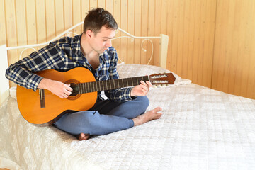Young man playing guitar and sitting on bed on weekend morning