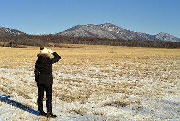 Fototapeta na wymiar Young woman in warm clothes standing in the field and looking at snowy mountains. winter, Russia.