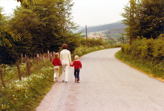 Vintage 1978 image of a young mother walking hand in hand on the side of the road with her daughter and son.
