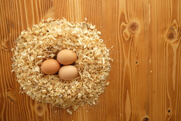 shell egg in sawdust on the wood, egg on the straw, eggs in the straw, fresh village eggs in the yellow sawdust, three village chicken eggs, wood background