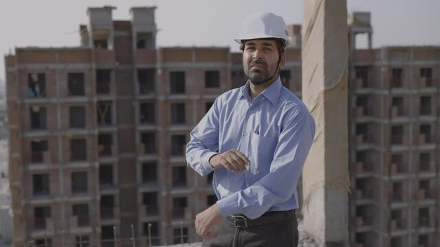 a rear view shot of a young male asian civil engineer standing on top of a under construction building turns around faces the camera moving towards him in motion