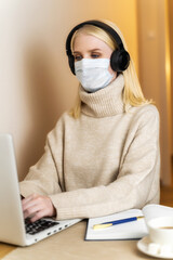 Girl in a protective mask and headphones works on a laptop