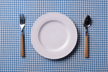 青いチェック柄の上の白い皿とカトラリー