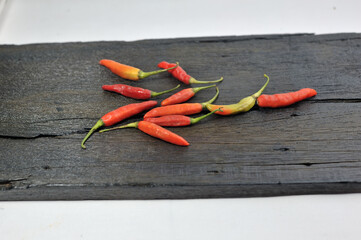 Some red chilies on a black wooden base and a bunch of red chilies in a plastic box on a white...