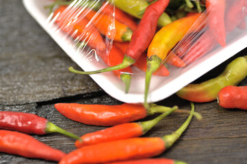 Some red chilies on a black wooden base and a bunch of red chilies in a plastic box