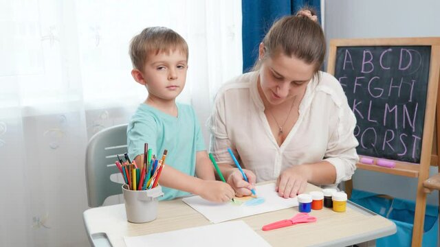 Little toddler boy with young mother drawing and painting with colorful pencils. Doing homework and edcucation with parents.