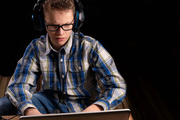 Boy with shirt and glasses doing homework on laptop with headset