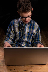 Child with glasses and shirt crunches looking behind laptop