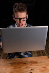 Child with glasses and shirt skeptically looking behind laptop