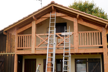 painter ladder painting the wooden beams and railings of the house