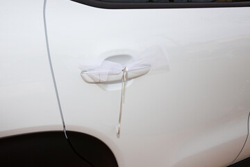 decorative ribbon hanging on the door of the bride white car at the wedding
