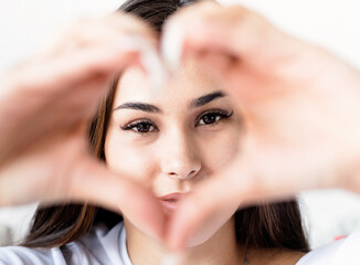 Fototapeta premium Young happy brunette woman in white t-shirt showing heart sign with her hands in front of face