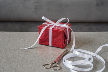 decorated gift box in red wrapped paper side view with a white ribbon and bow on a gray table...