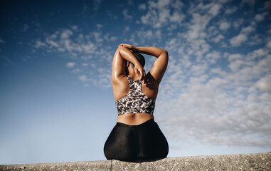 Plus size woman sitting on wall and stretching arms