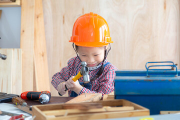Asian little girl is designing and constructing a wooden house in carpentry shop. Learning, family, activities concept.