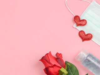 flat lay of red gitter hearts, medical face mask, alcohol sanitizer gel and red rose on pink background. COVID19 prevention, new normal and Valentine's day concept.