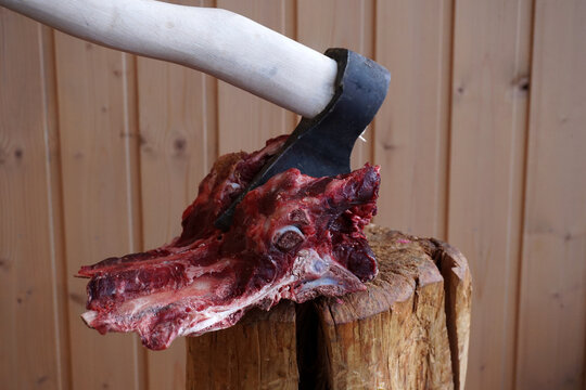 A piece of meat with bones chopped with an ax on a stump.
