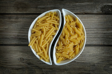 Raw pasta of two kinds in a curved white dish on wooden boards. Vintage style. Selective focus. View from above