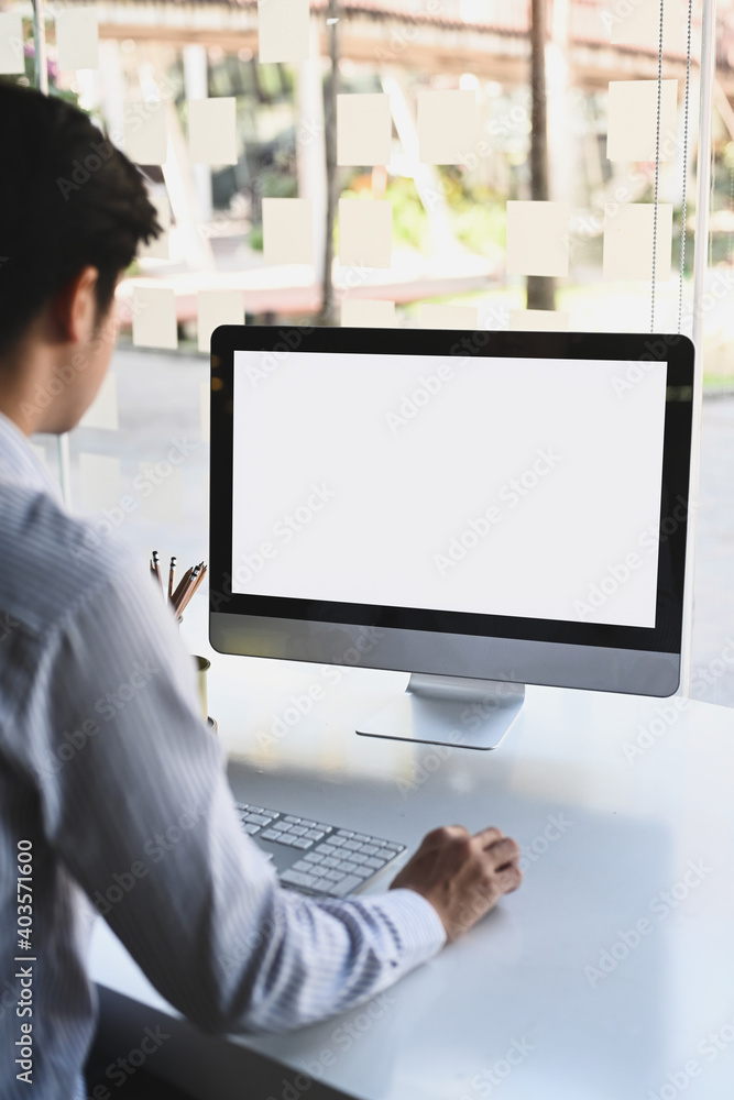 Poster rear view of businessman working with computer while sitting in modern office.
