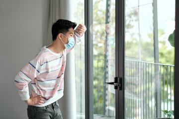 Young man during coronavirus pandemic wearing face mask indoors at home for social distancing