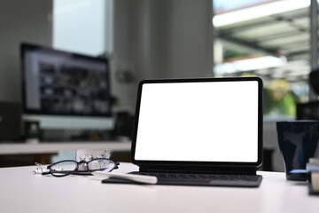 Mock up tablet computer with blank white screen on office desk in modern office.