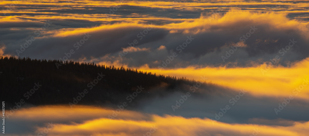 Wall mural waves of clouds rolling over the top of the mountain illuminated by the rising sun