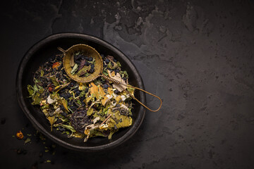 Mixture of teas, dried organic tea herbs and fruits in bowl with tea strainer