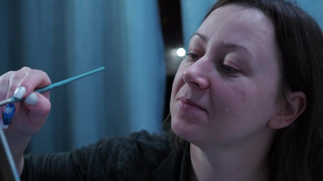 the artist draws with a brush on the canvas. home studio of fine arts. smiling at the camera.