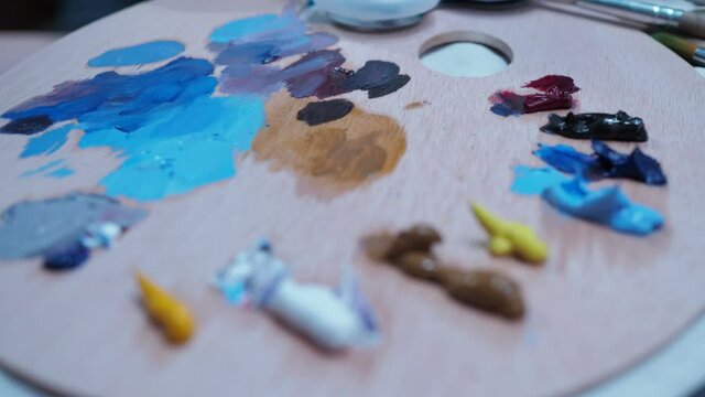 the girl stirs the oil paints with a brush from the palette. close-up.