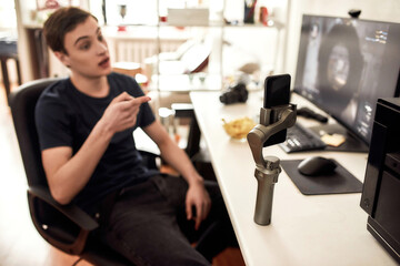 Fototapeta premium Teenage guy using smartphone on a tripod while playing game and recording video. Blogging, technology concept