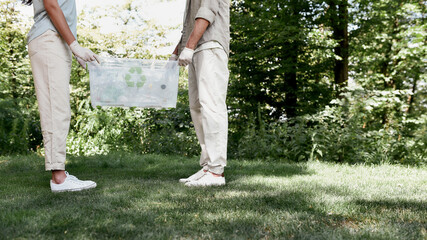 Recycling concept. Cropped shot of two volunteers holding recycle bin with plastic waste while standing in the forest or park